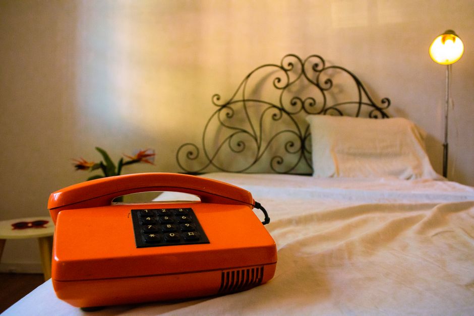 Cozy bedroom with a vintage orange telephone on a white bedspread near a decorative headboard.